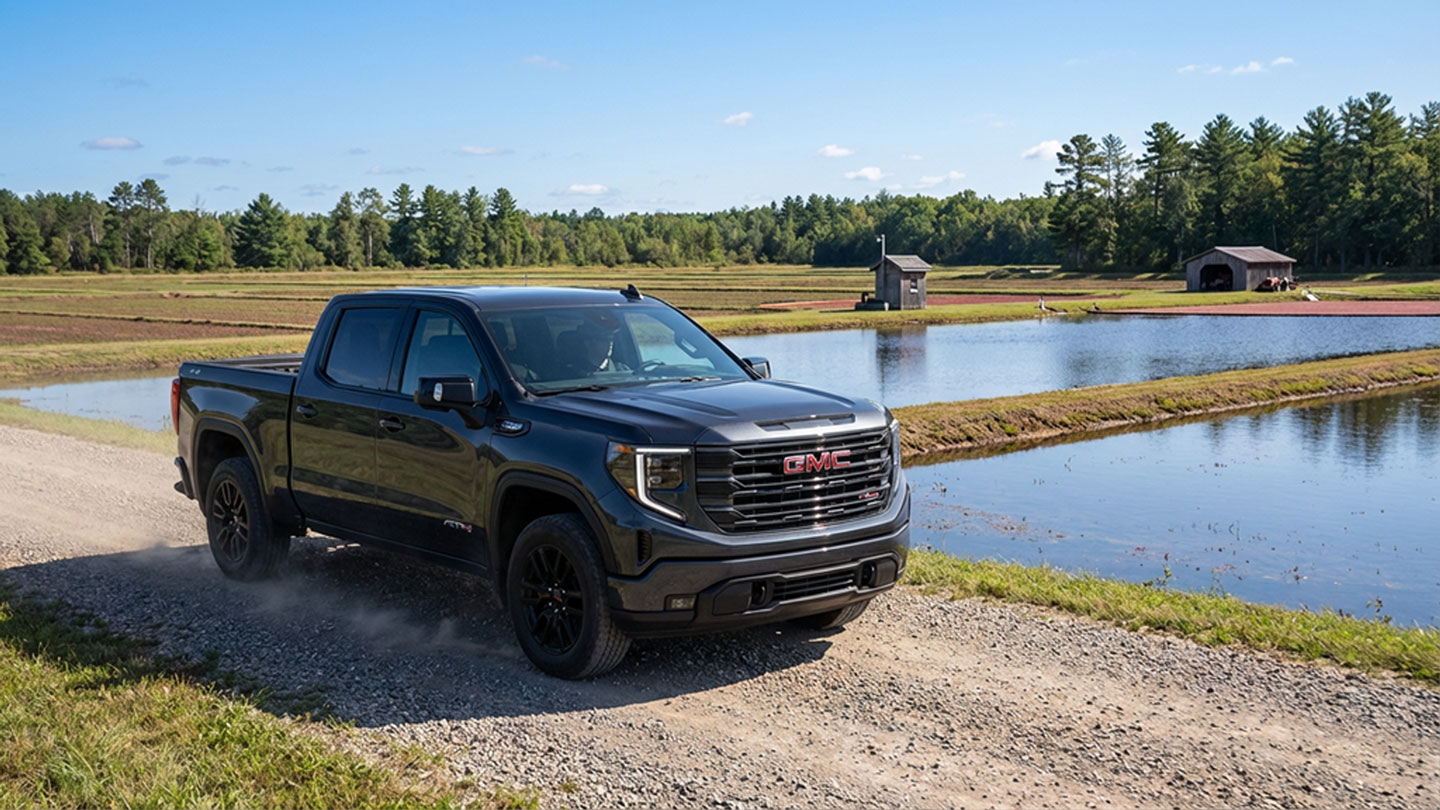 2026 GMC Sierra 1500 AT4 driving beside a Central Wisconsin cranberry bog under bright blue skies