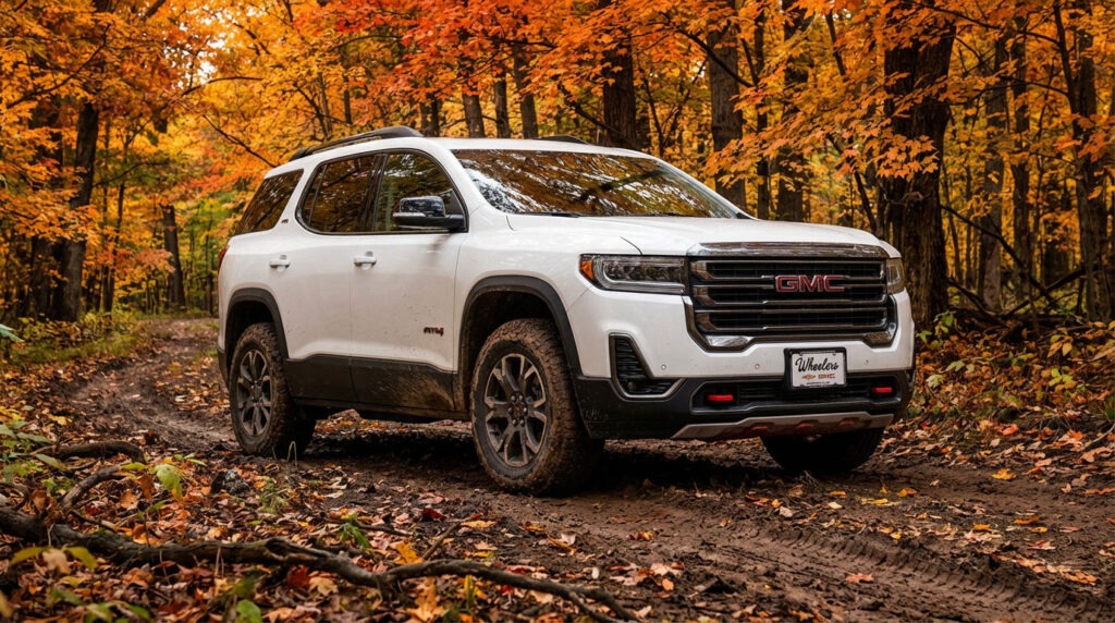 2026 GMC Acadia AT4 on a muddy two-track trail through a Wisconsin hardwood forest in peak fall foliage with orange and red maple canopy overhead and light mud on the lower doors and tires