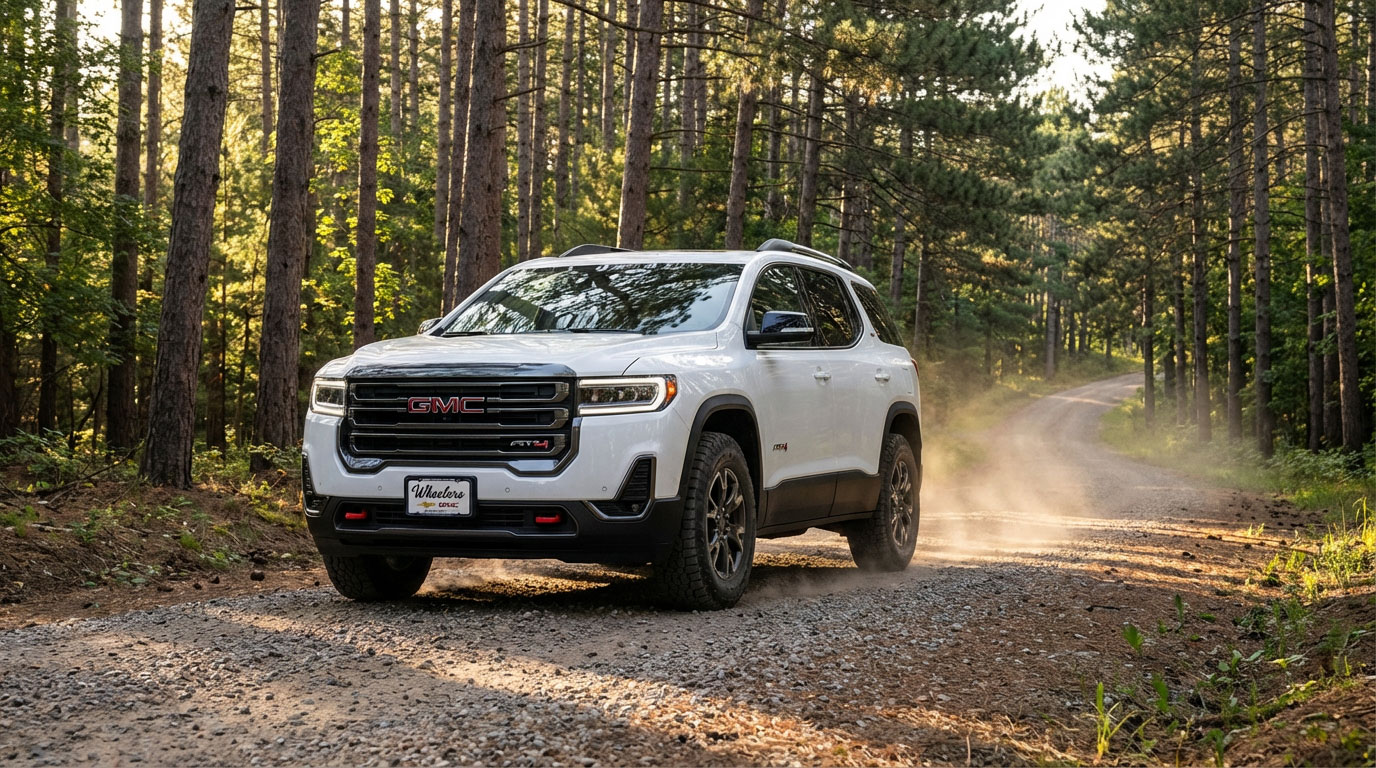 2026 GMC Acadia AT4 on a gravel forest road in a Wisconsin state forest with morning light filtering through pine trees and AT4 badging visible