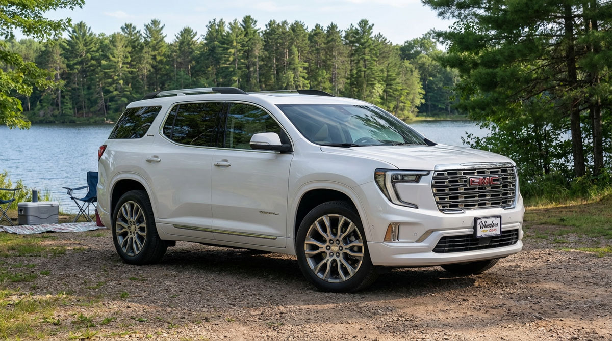 2026 GMC Acadia parked at a Wisconsin lakefront state park with calm blue water and green pine trees on a bright summer afternoon