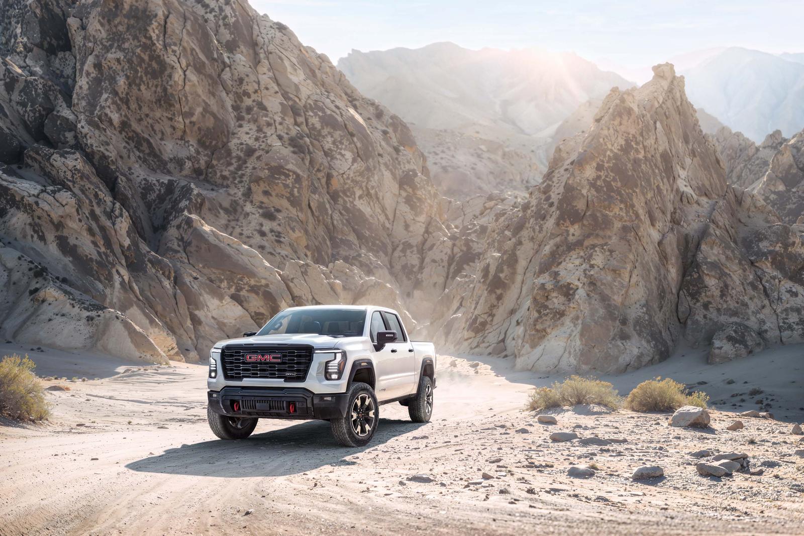 White 2027 GMC Sierra 1500 AT4 with red front tow hooks driving through a rocky desert canyon