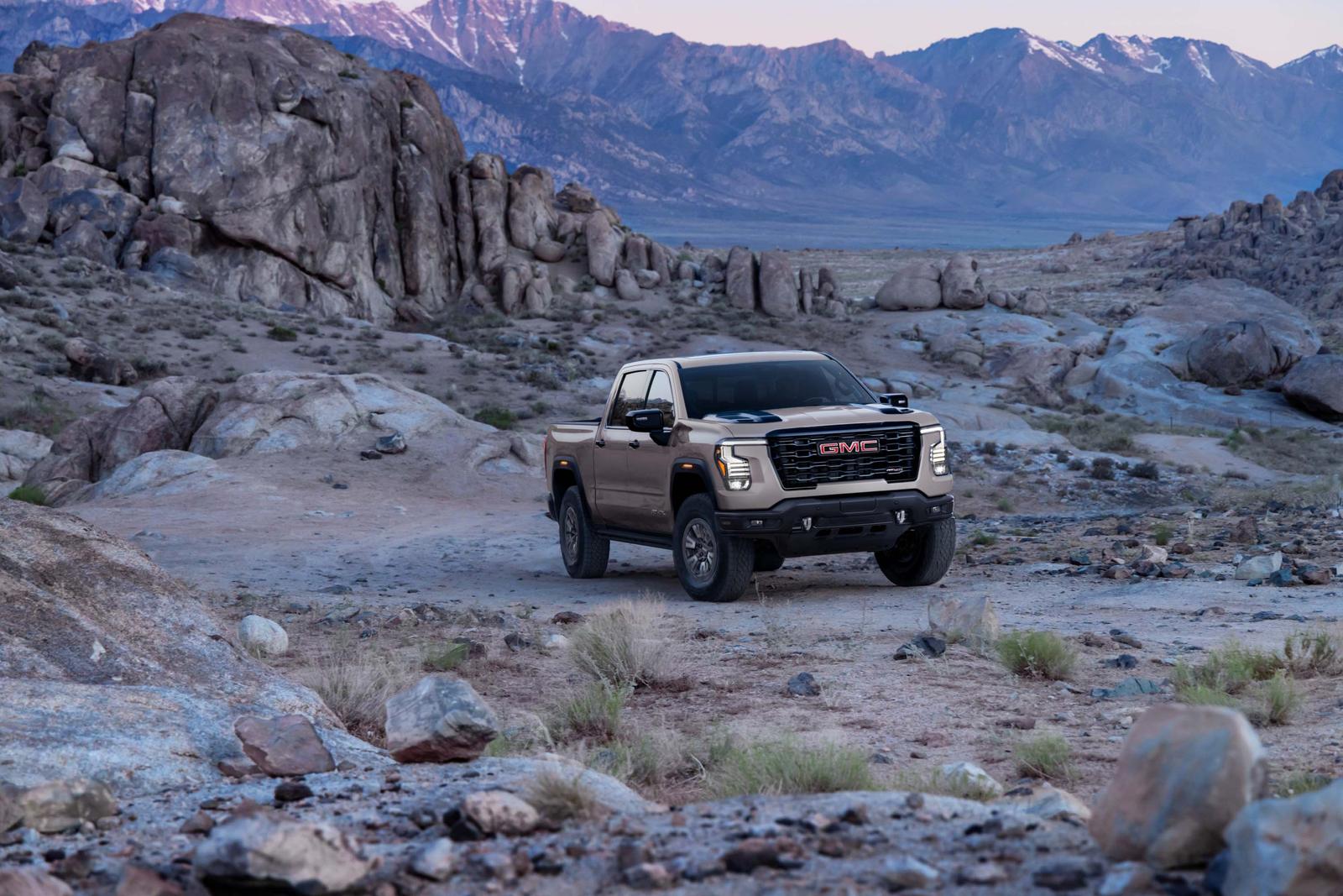 Tan 2027 GMC Sierra 1500 AT4X on a rocky desert trail with snow-capped mountains behind it