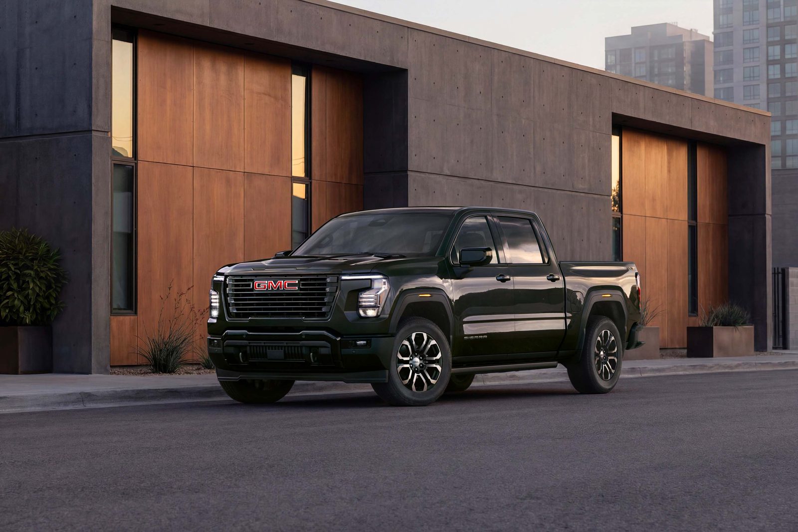 Black 2027 GMC Sierra 1500 Crew Cab showing the new vertical grille and 7-shaped LED headlamps, parked in front of a modern building