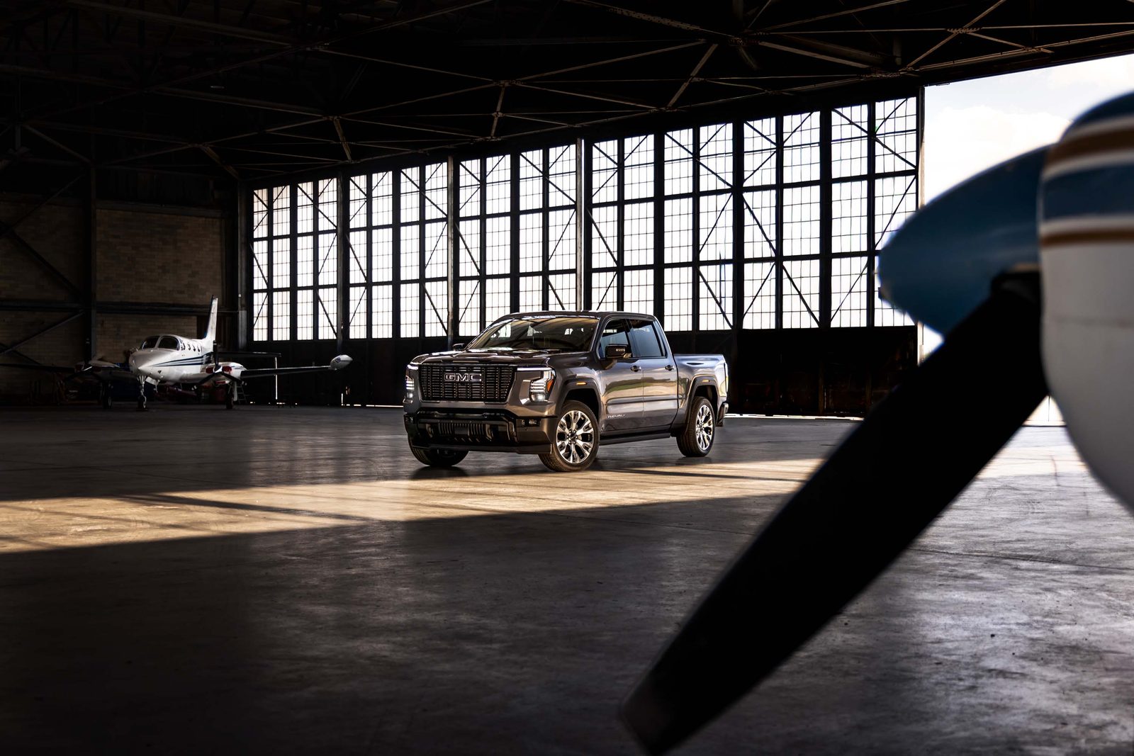 Dark gray 2027 GMC Sierra 1500 Denali Ultimate parked inside an airplane hangar next to a small private jet