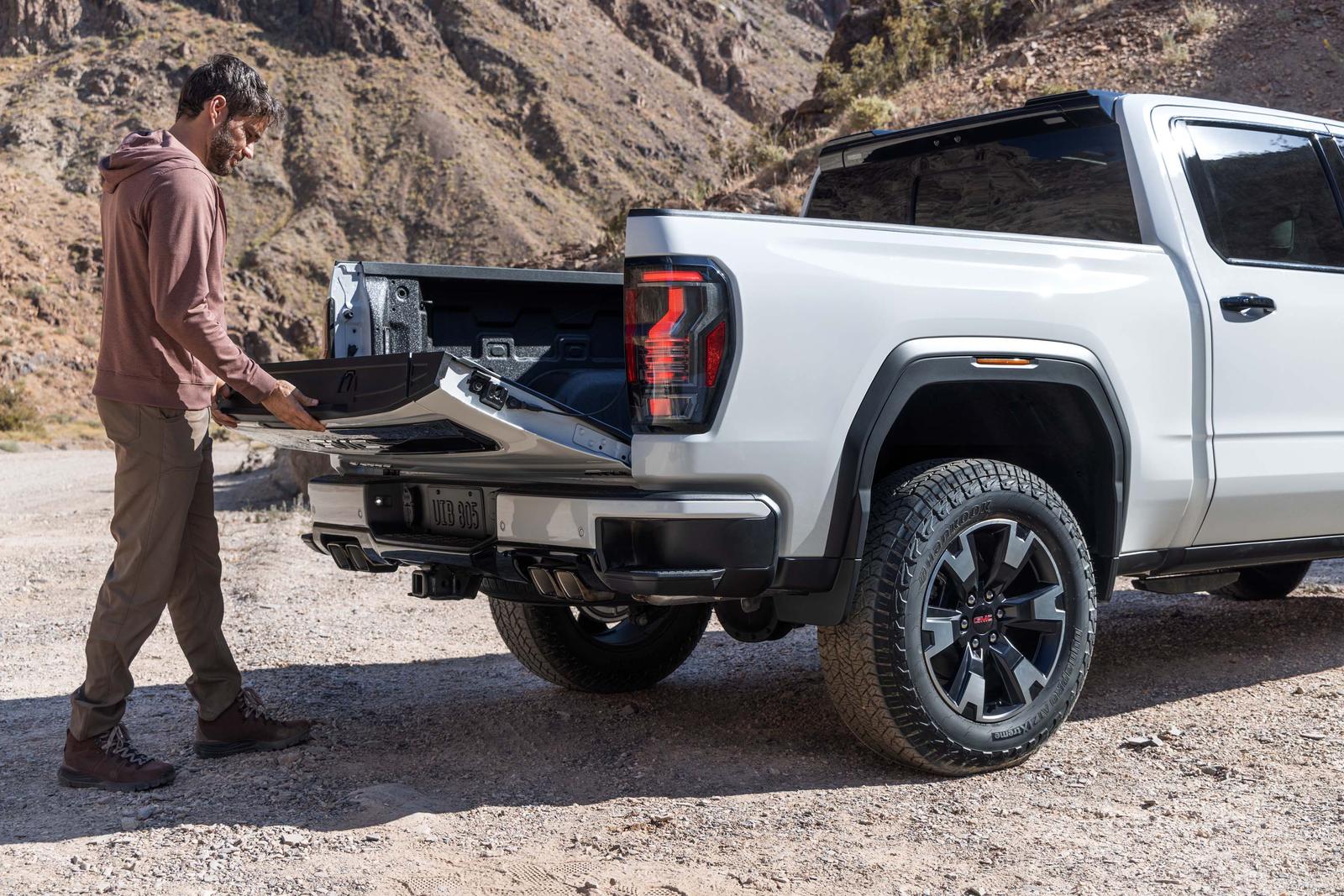 Man folding down the MultiPro Tailgate on a white 2027 GMC Sierra 1500 at a gravel trailhead
